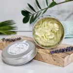 Baume fouetté dans un pot ouvert gris, avec une crème fouetté sans micas (de couleur jaune), posé sur un support en bois
